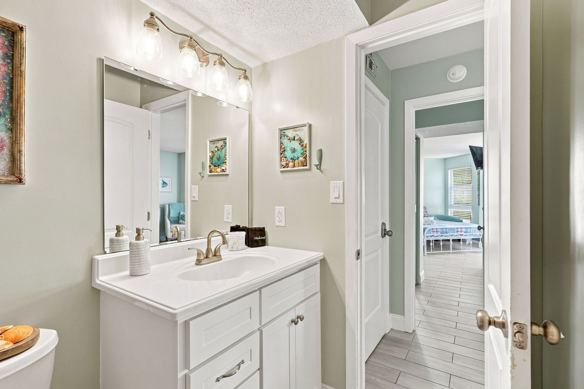 Clean and well-lit bathroom space complete with a traditional vanity, large mirror, and direct view down the hallway.