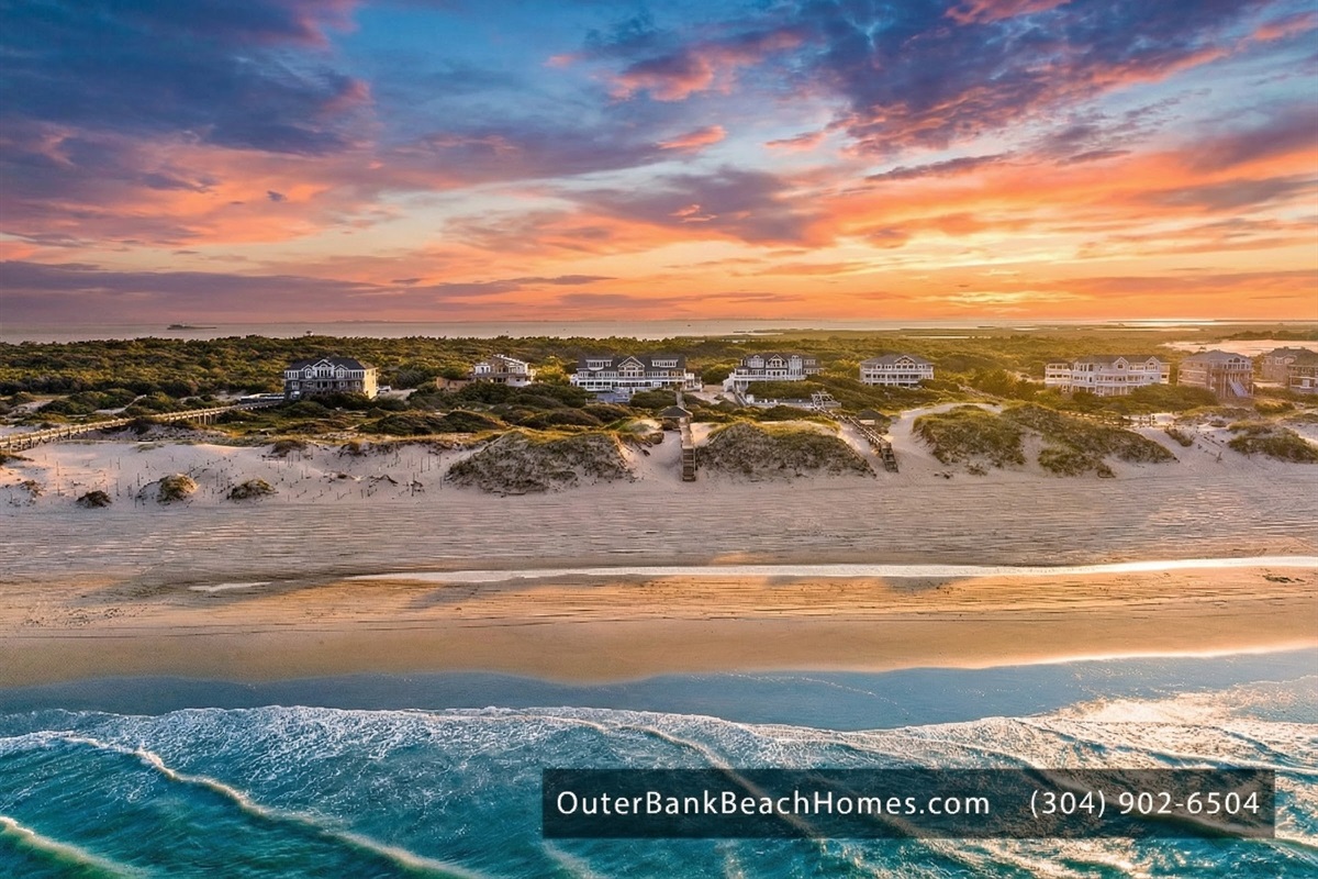 Aerial view of the coastline and beach homes under a vibrant sunset.