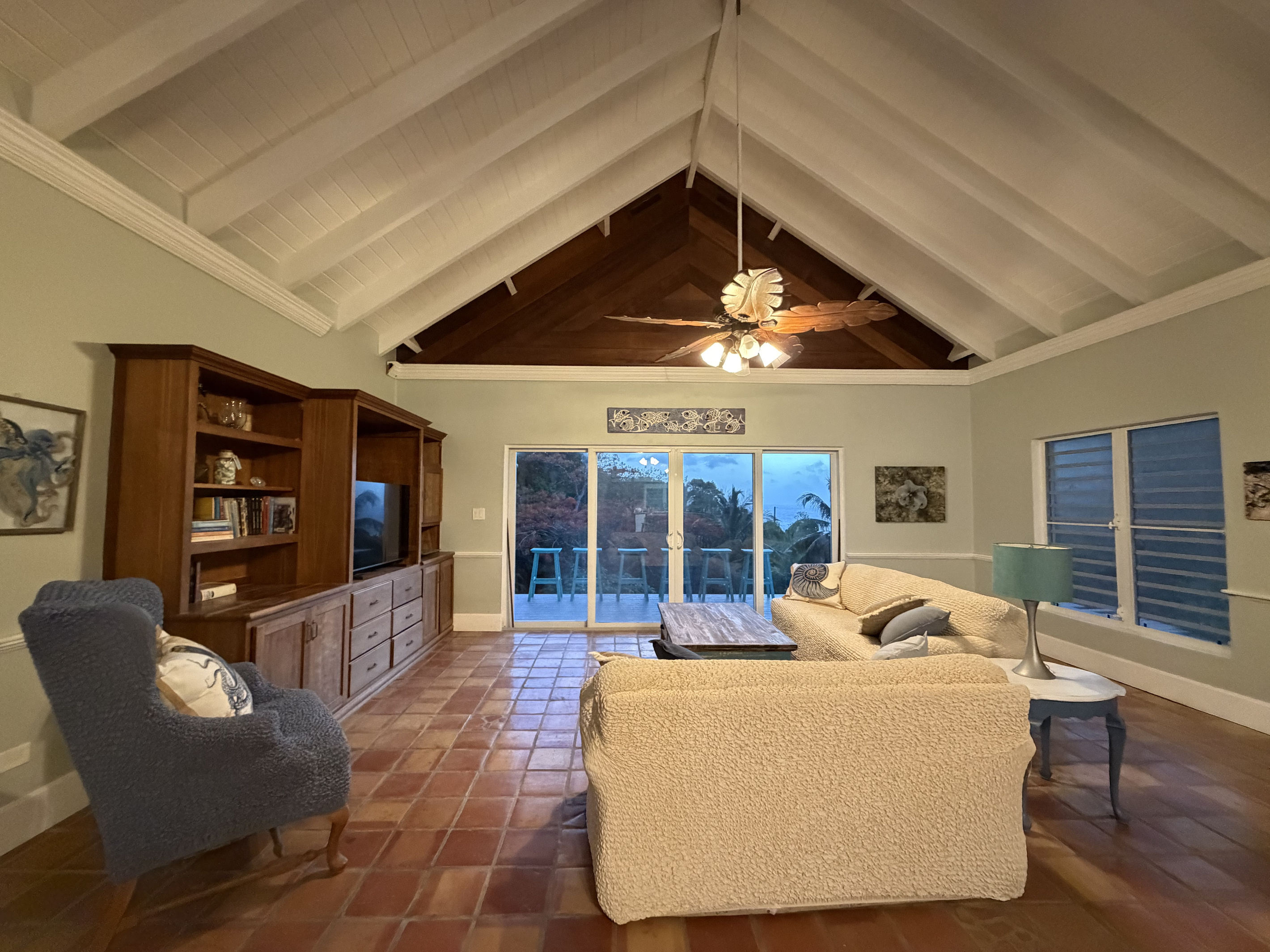 Soaring vaulted ceilings, rich wood accents, and a unique tropical leaf ceiling fan set a relaxed island vibe. Plenty of comfortable seating options gathered around a TV entertainment center and rustic coffee table.
