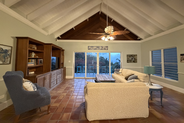 Soaring vaulted ceilings, rich wood accents, and a unique tropical leaf ceiling fan set a relaxed island vibe. Plenty of comfortable seating options gathered around a TV entertainment center and rustic coffee table.