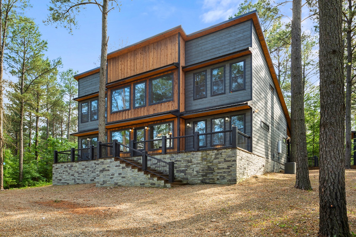 Modern cabin featuring large windows and wooden accents standing amid tall trees.