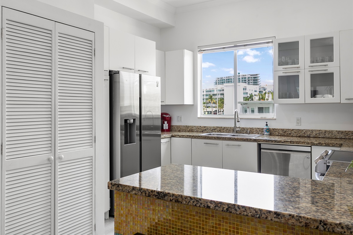 Mosaic tiled kitchen with modern appliances and breakfast counter. LG laundry tower behind closet doors