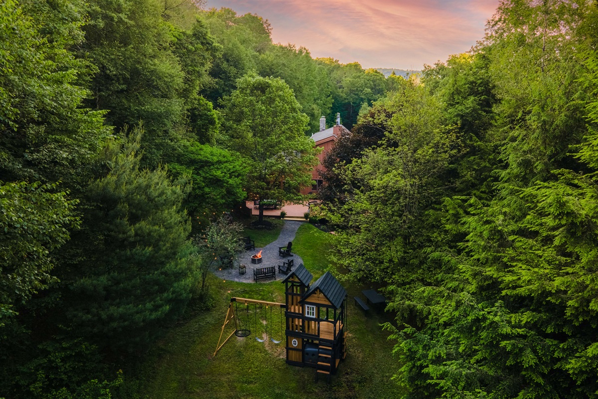 An inviting aerial view of the backyard fire pit, playground, and pathways.