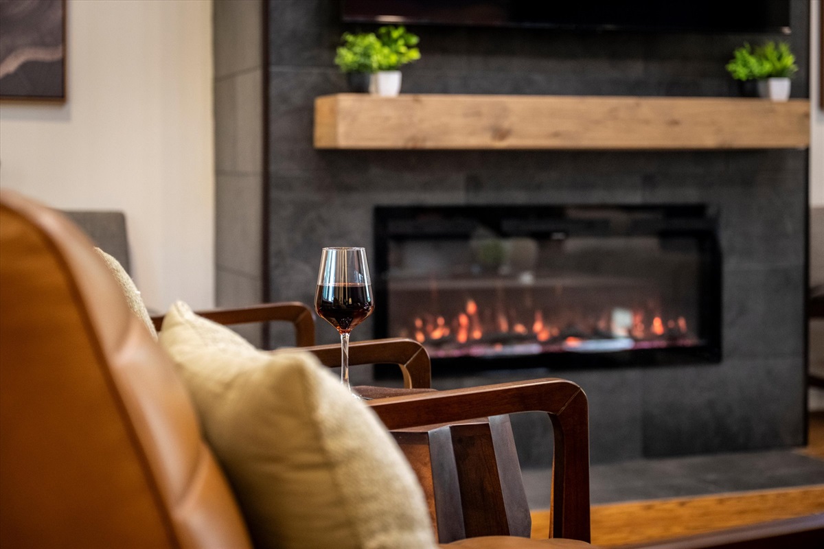 Cozy up beside the sleek fireplace, framed by natural textures and local artwork. It’s an inviting corner for quiet moments, warm conversations, and mountain vibes indoors.