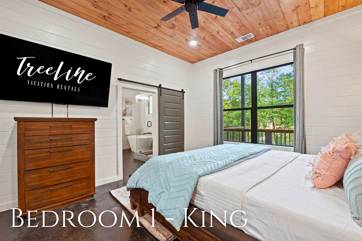 A serene bedroom featuring a king-size bed with direct access to a modern en-suite bathroom, framed by large windows showcasing woodland views.