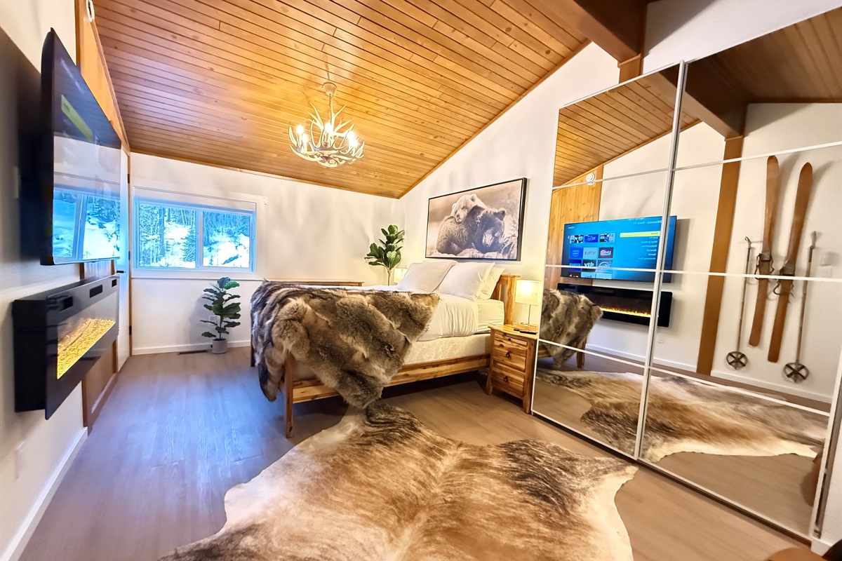 A romantic loft bedroom suite with alpine decor, a 65" TV, electric fireplace, closet and dresser storage. 