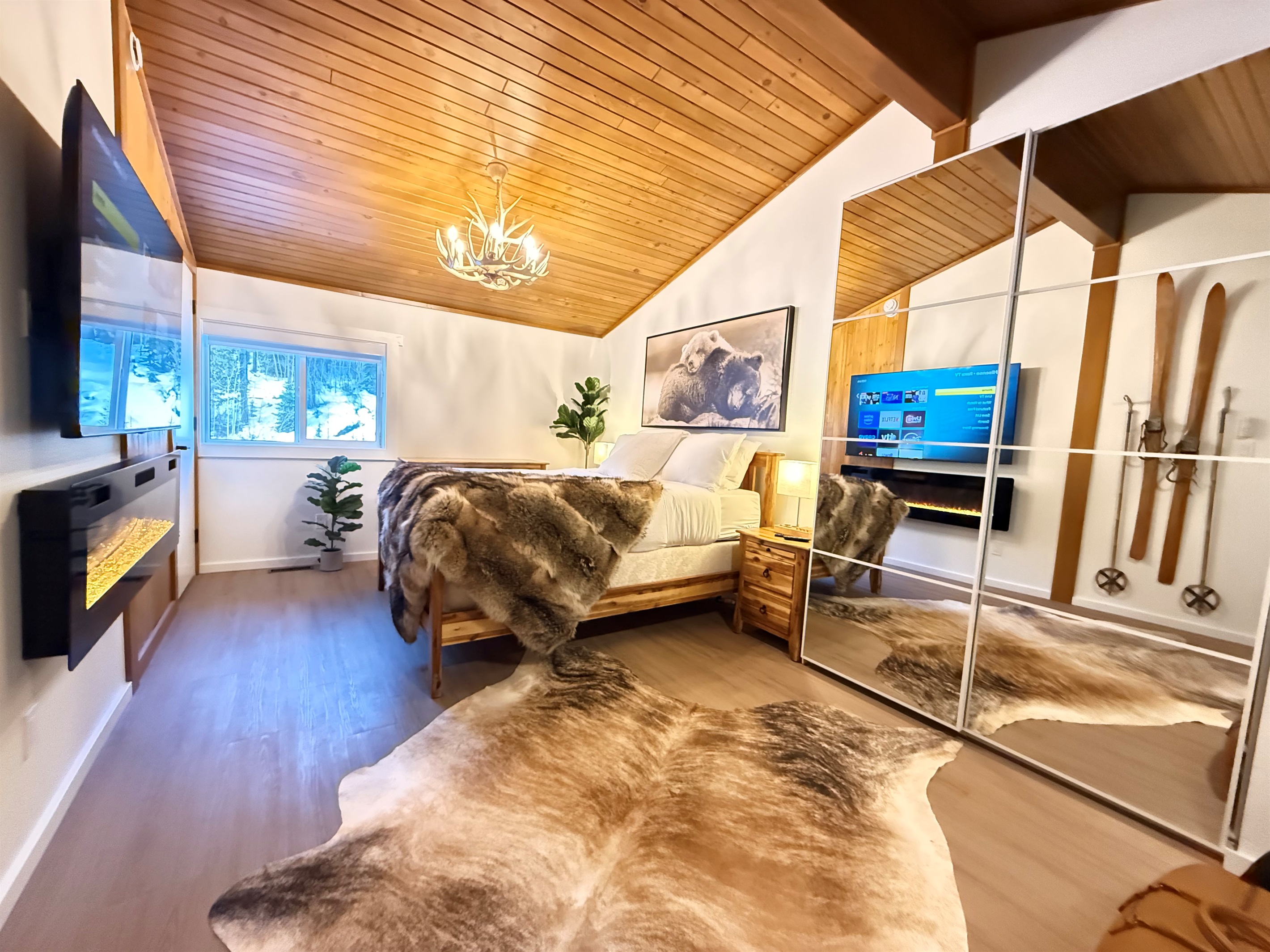 A romantic loft bedroom suite with alpine decor, a 65" TV, electric fireplace, closet and dresser storage. 