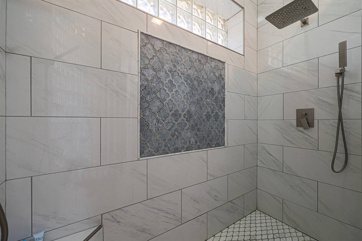 A beautifully tiled rainfall shower with custom inset and handheld fixture creates a serene and rejuvenating experience.