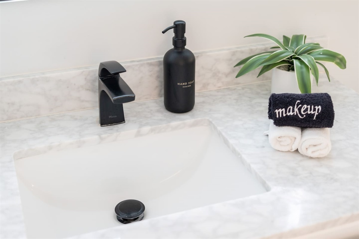 Sleek vanity with a marble top, matte black faucet, hand soap, and a thoughtful "makeup" towel detail.