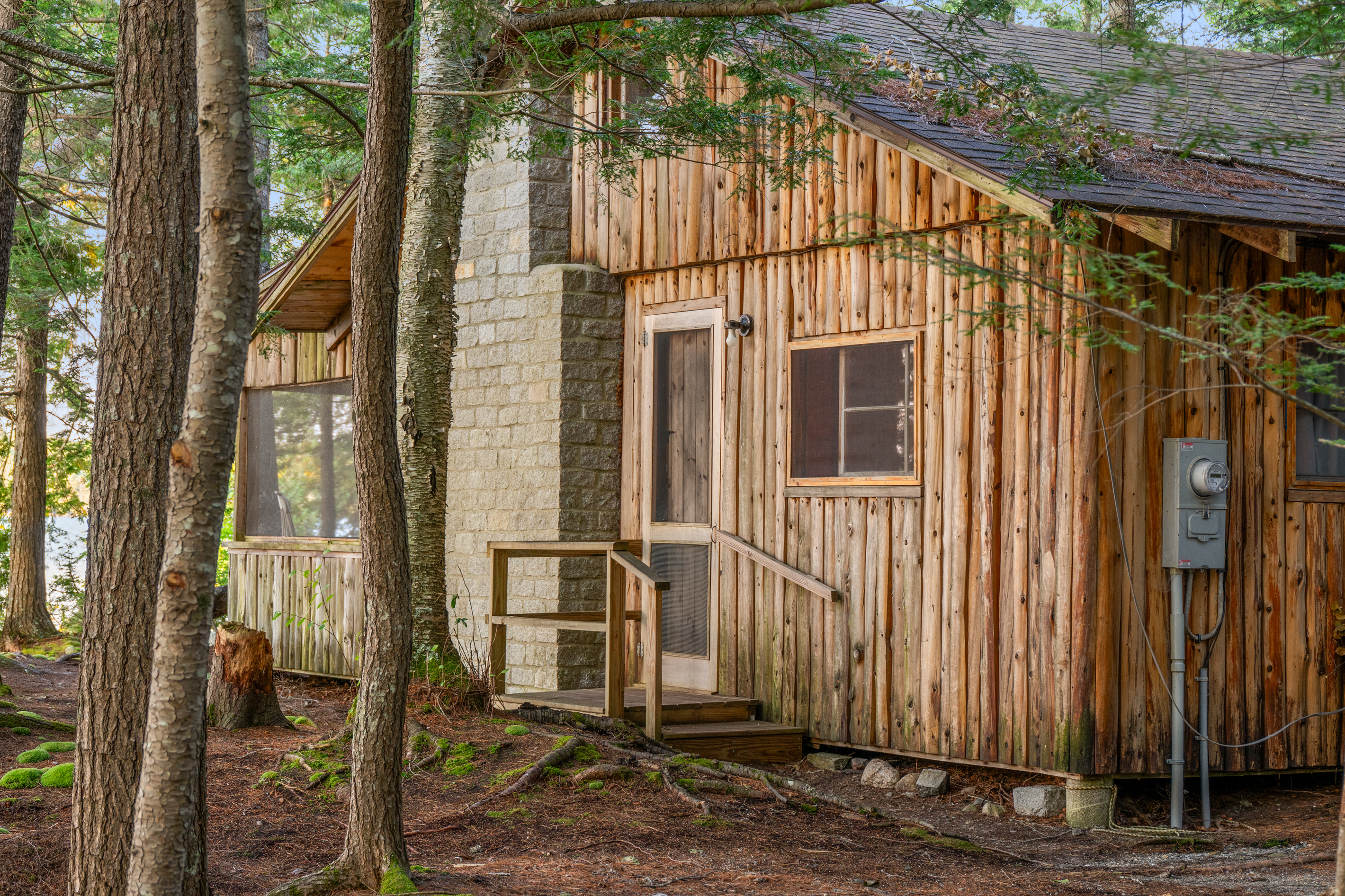 The main entrance at Loonrise Point on Beech Hill Pond in Otis, ME. Wooden steps lead right to the door of this historic cedar camp, complete with its original stone chimney and quiet pine surroundings. Just 40 minutes to Acadia National Park!