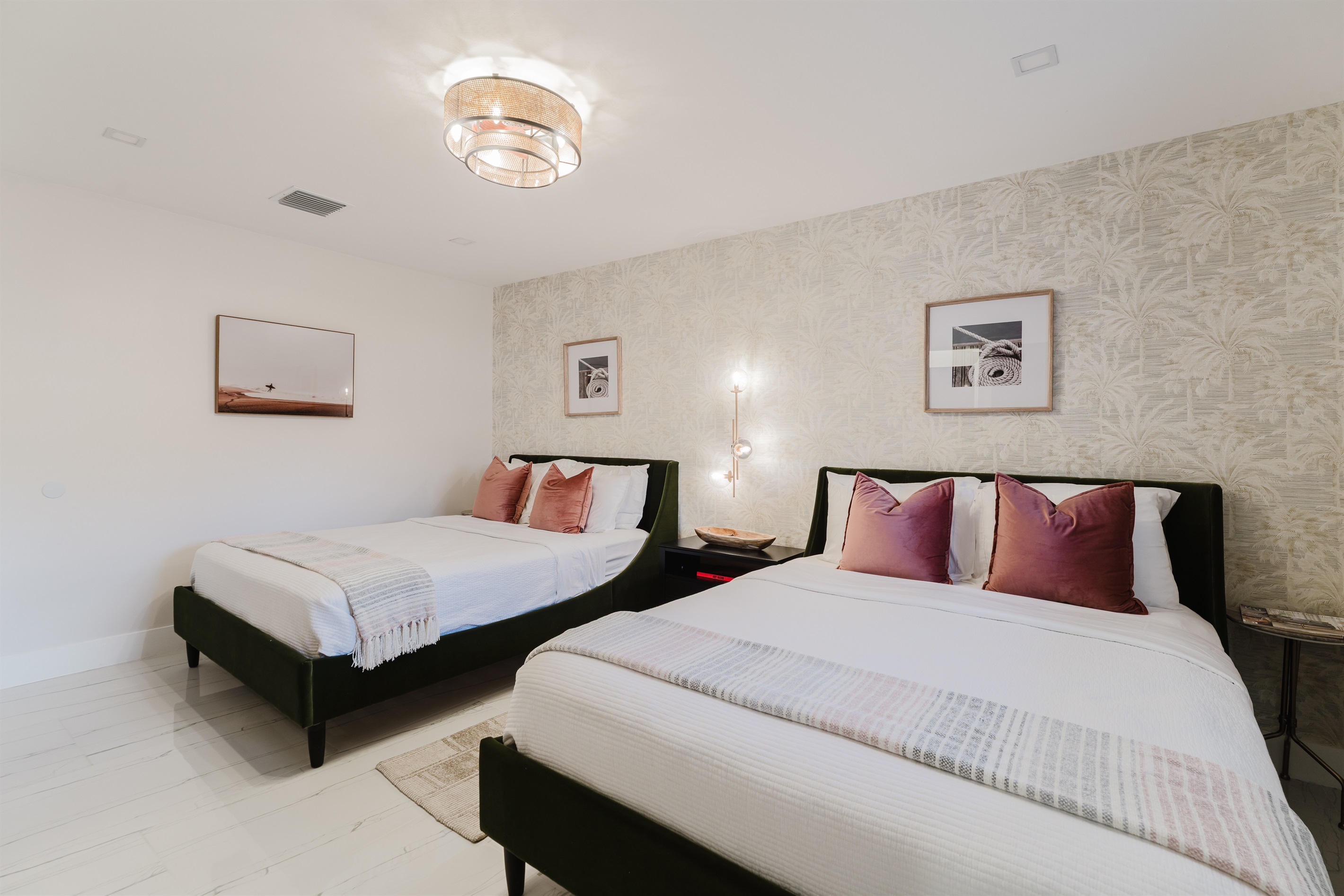Bright coastal suite with two queen beds, private ensuite bath, smart TV, blackout bamboo shades, and a rattan ceiling fan—ideal for families or shared stays.