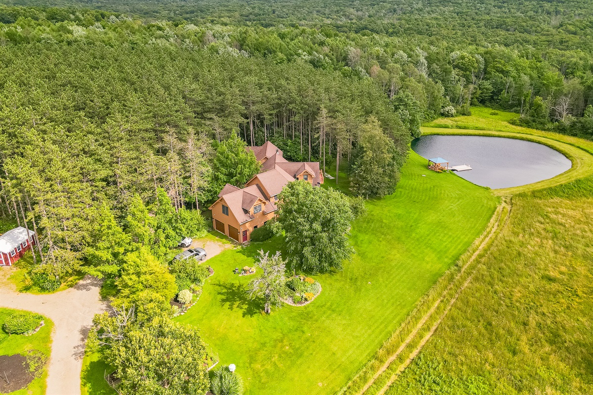 Stunning bird’s-eye view of the home nestled in trees, complete with a sparkling pond and open green fields.