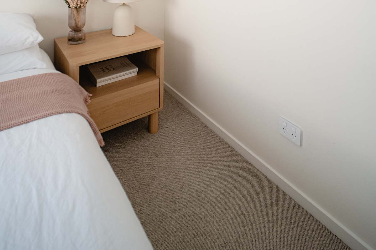A cosy bedroom corner with soft neutral tones, elegant floral artwork and thoughtful bedside touches.