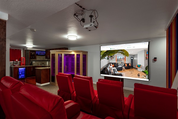 Private theater-style lounge with red recliner seating, a large projector screen, sauna, and kitchenette, perfect for movie nights and relaxing with your group.