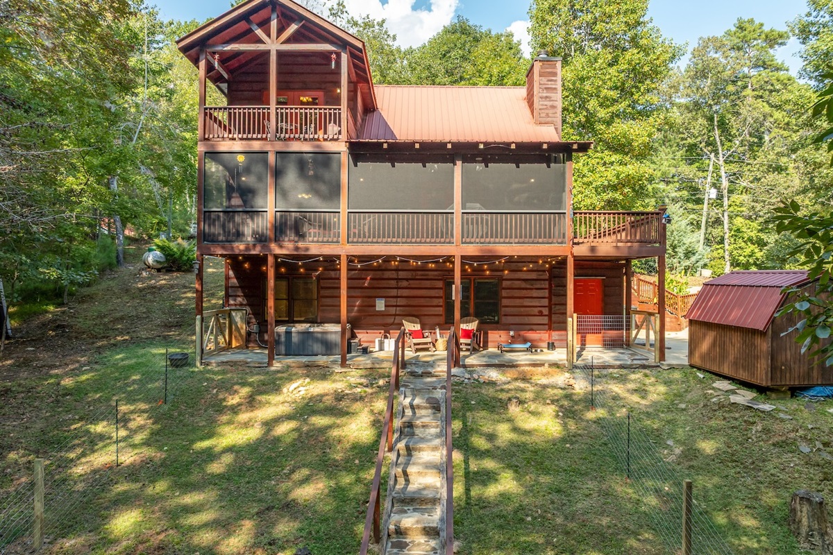 From above, the drone captures a peaceful haven — a private porch off the king bedroom and a screened-in porch with a gentle bench swing and BBQ. Down back, the hot tub bubbles beside an elevated dog bed, complete with water bowl for your furry travel bud!
