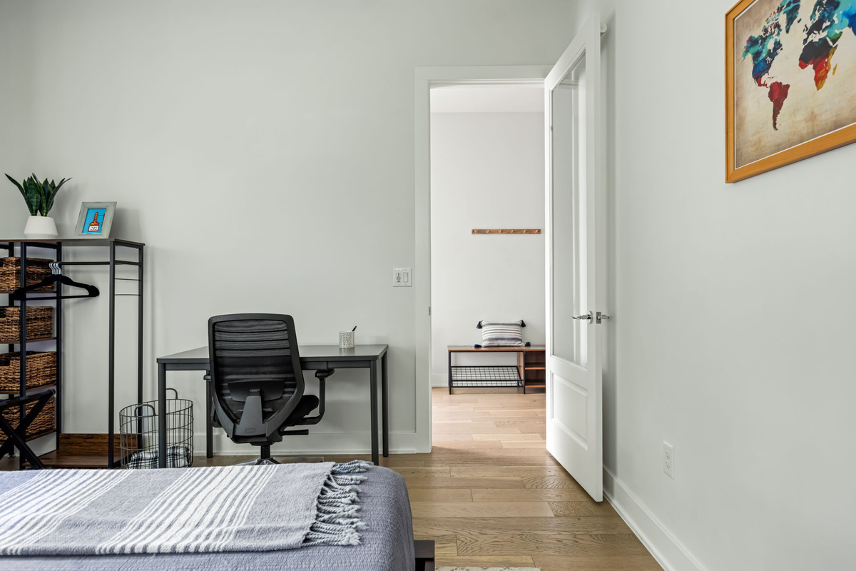 Comfortable guest bedroom featuring soft bedding, a modern desk setup, and easy access to the hallway and additional living spaces.