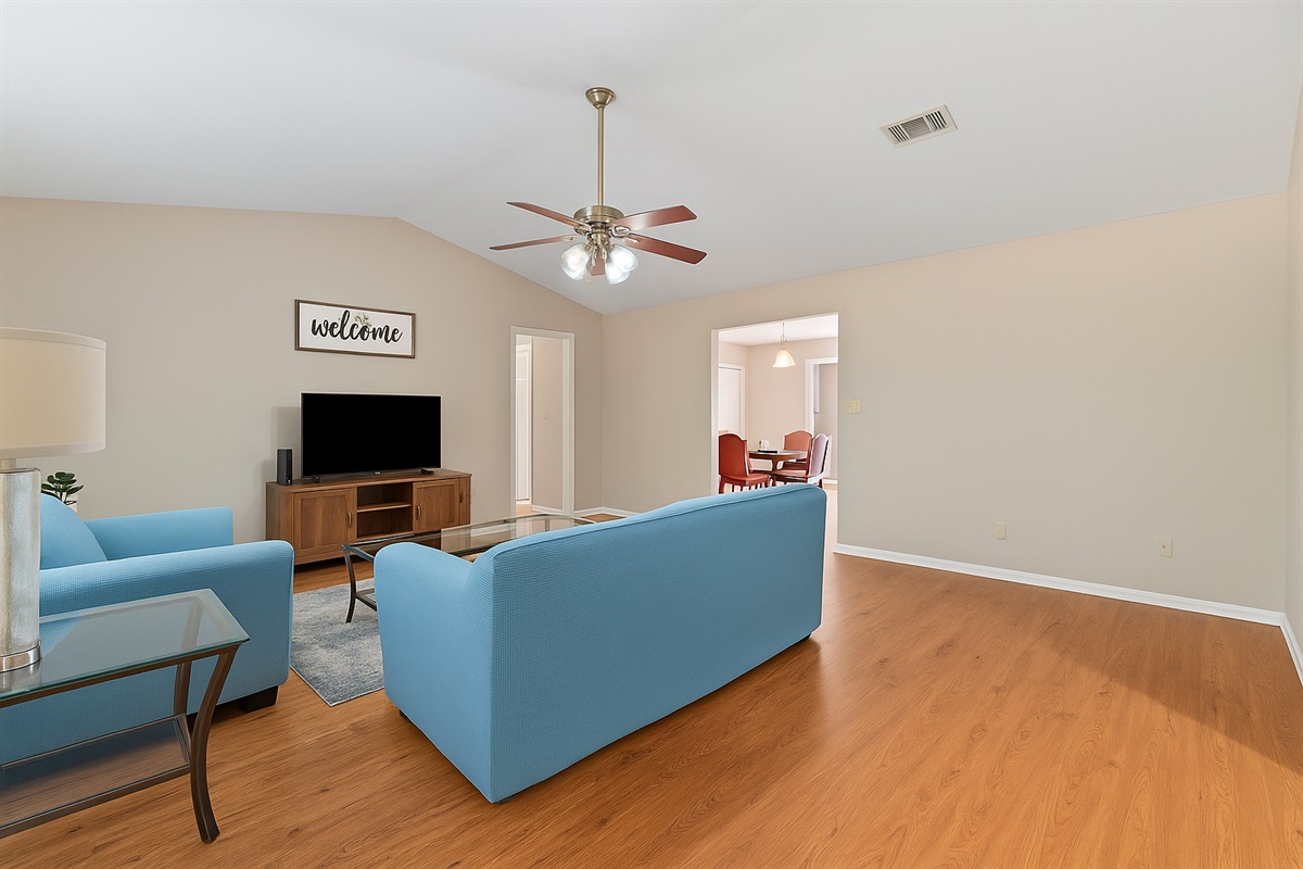 Bright and welcoming living room with stylish blue sofas, a TV, and ceiling fan—perfect for relaxing after a day out.