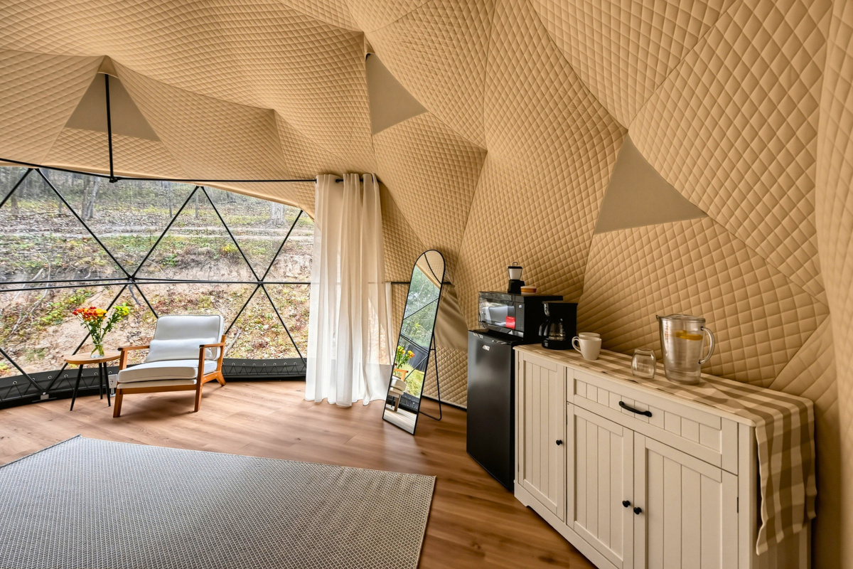 Explore the dome’s cozy interior, with a mirror, mini fridge, dishes, and a comfortable seating area.