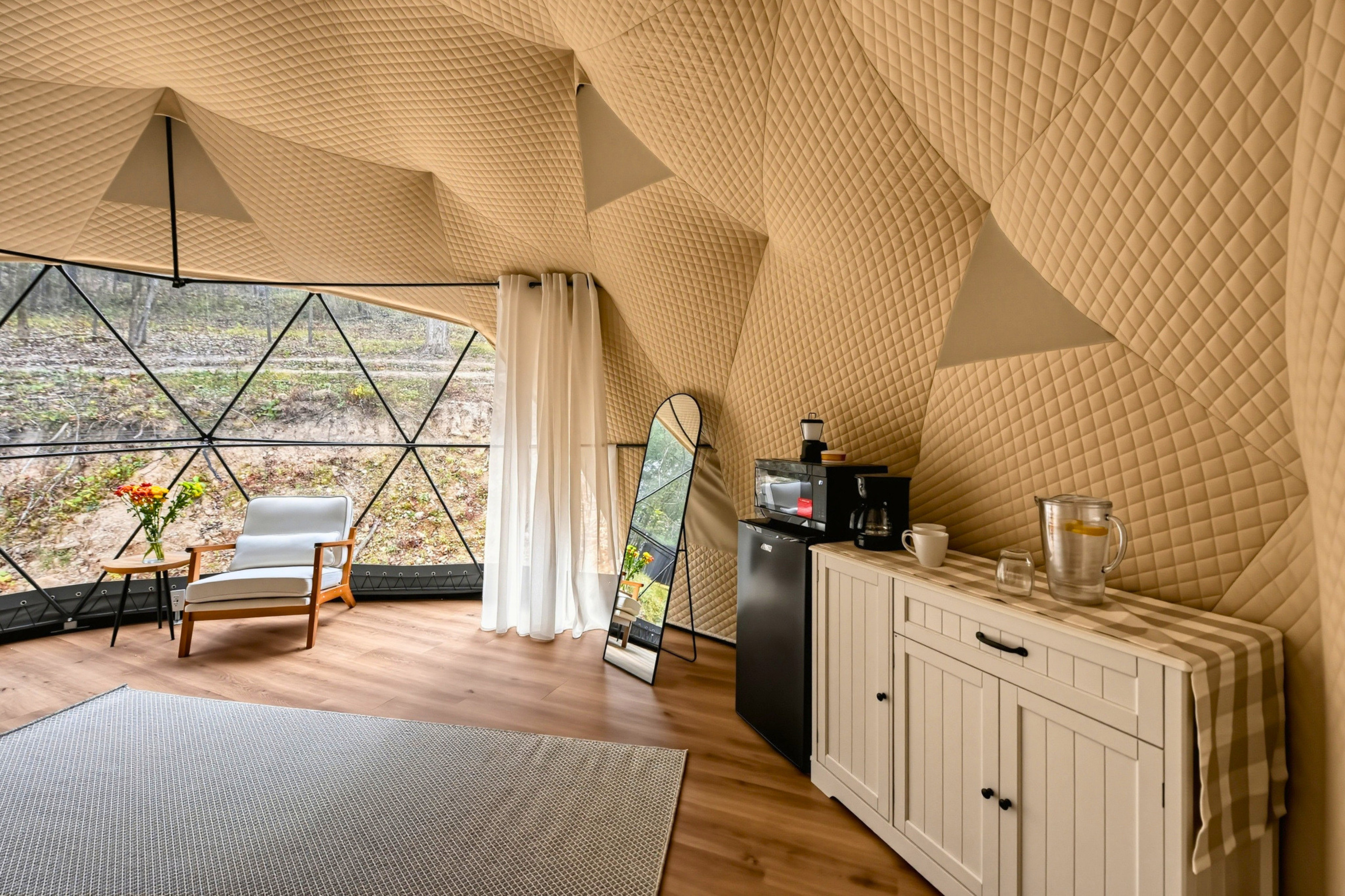 Explore the dome’s cozy interior, with a mirror, mini fridge, dishes, and a comfortable seating area.