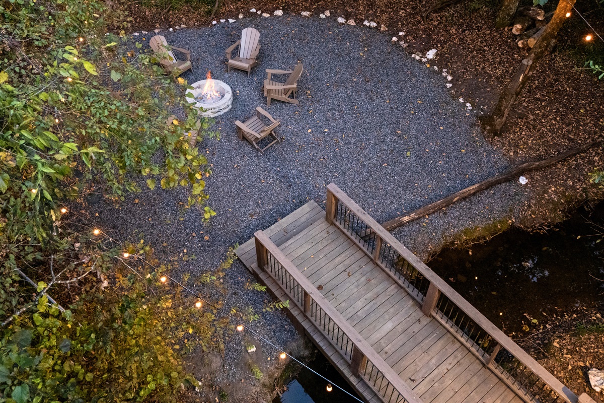 A small wooden bridge adds a charming touch as it crosses over the landscaped outdoor area near the fire pit.