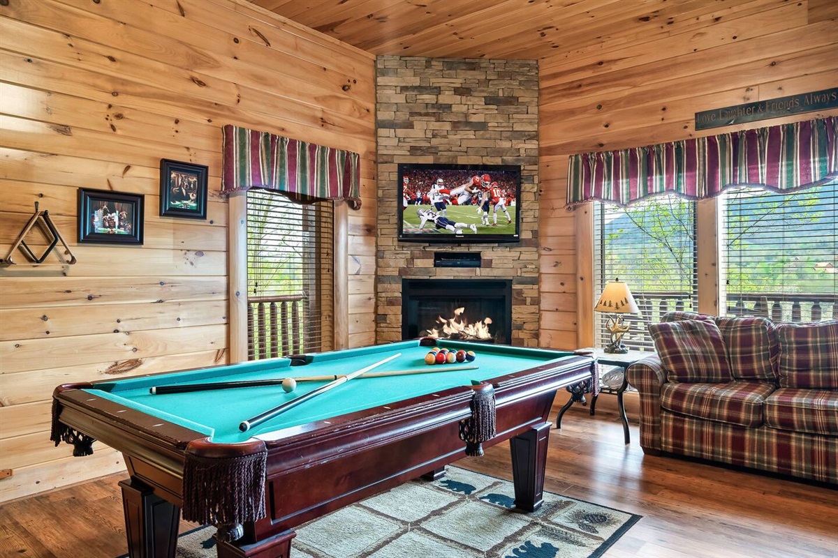 Downstairs game room which doubles as the 4th bedroom.Game room includes pool table, multicade, TV, and access to the downstairs wrap around porch.Pull out sofa pictured.(Fireplace is electric and for decorative purposes only).