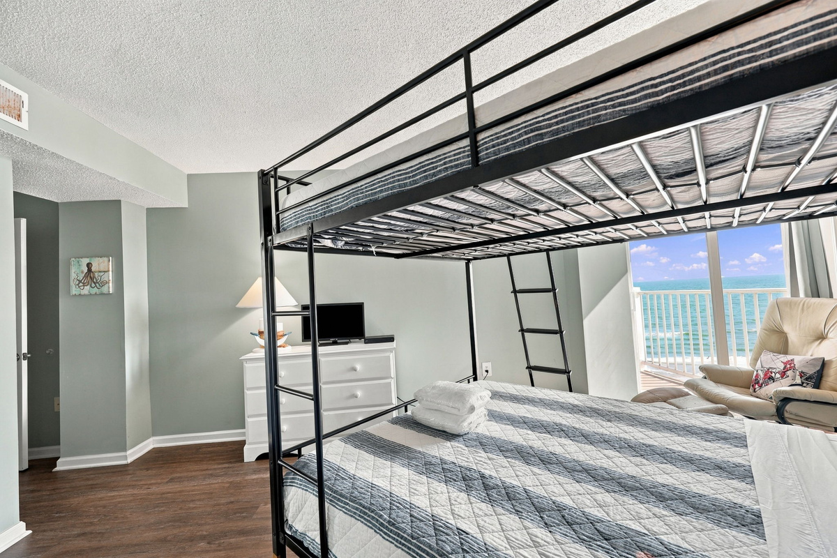 Bright and airy bedroom featuring a Queen-over-Queen bunk bed with direct access to the ocean-view balcony.