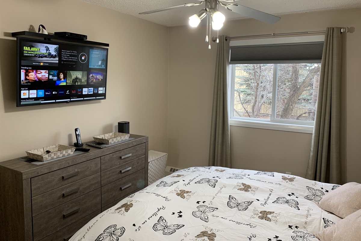 Second bedroom has large mirrored closet, queen bed set, dresser, end table and smart TV and Sonos speaker.