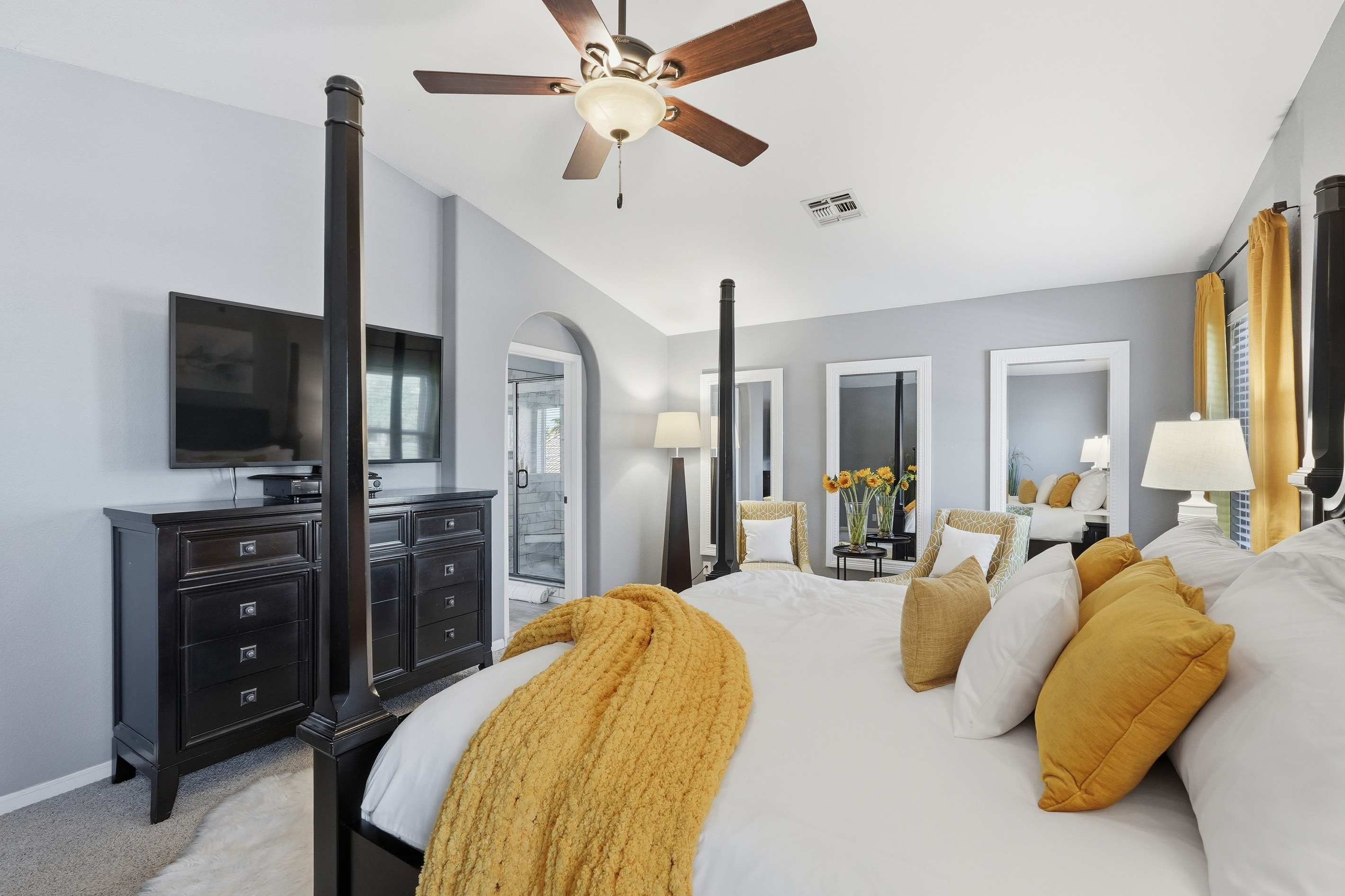 Primary bedroom with king bed, four-poster frame, sitting area, ceiling fan, and plenty of natural light.