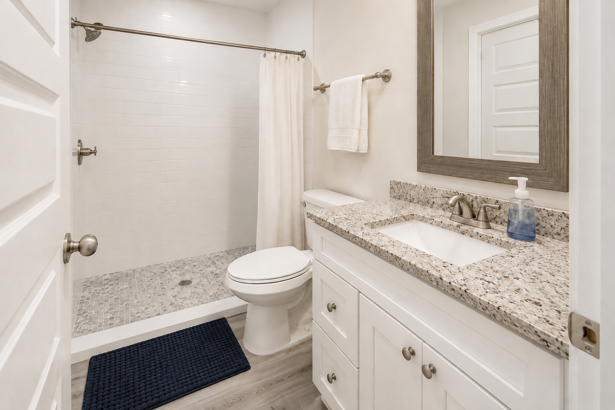 The walk-in shower rinses off beach days in style — subway tile to the ceiling, a pebble-stone floor underfoot, and a granite counter with room for the whole sunscreen lineup. Sand stays here, never in the sheets.