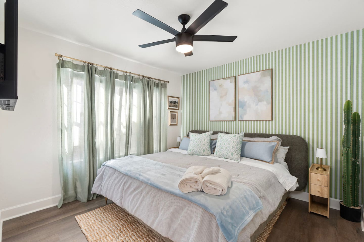 Bright guest bedroom with green striped accent wall, soft linens, and natural light—a calming retreat with thoughtful style.