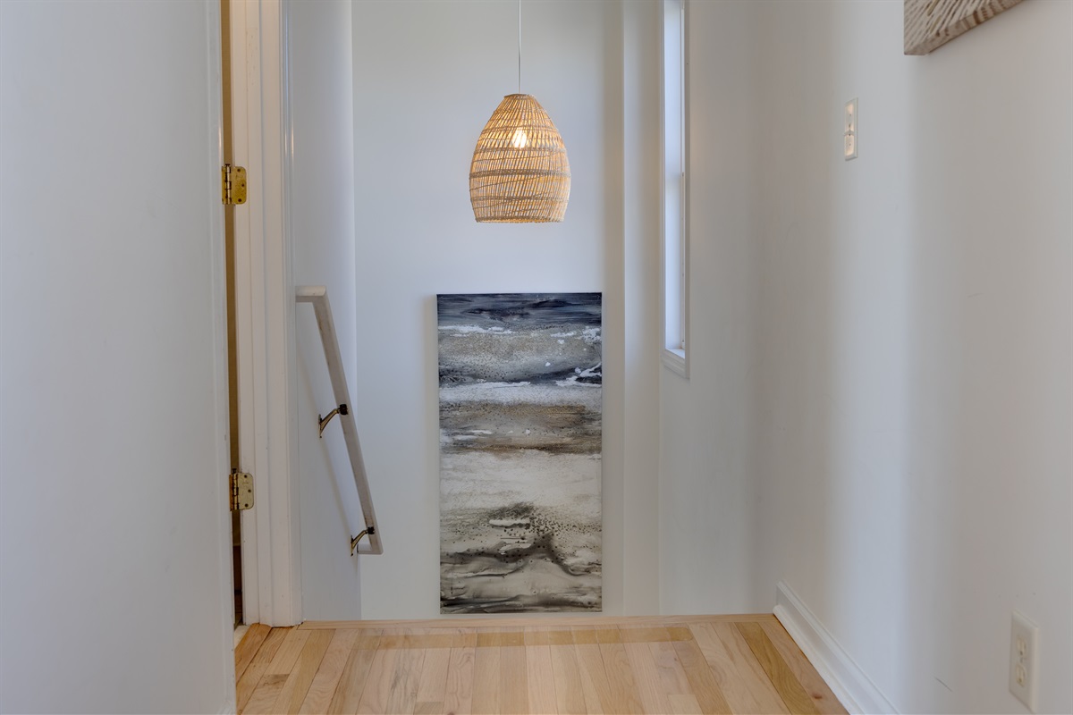Light-filled stair landing with warm wood floors and coastal artwork