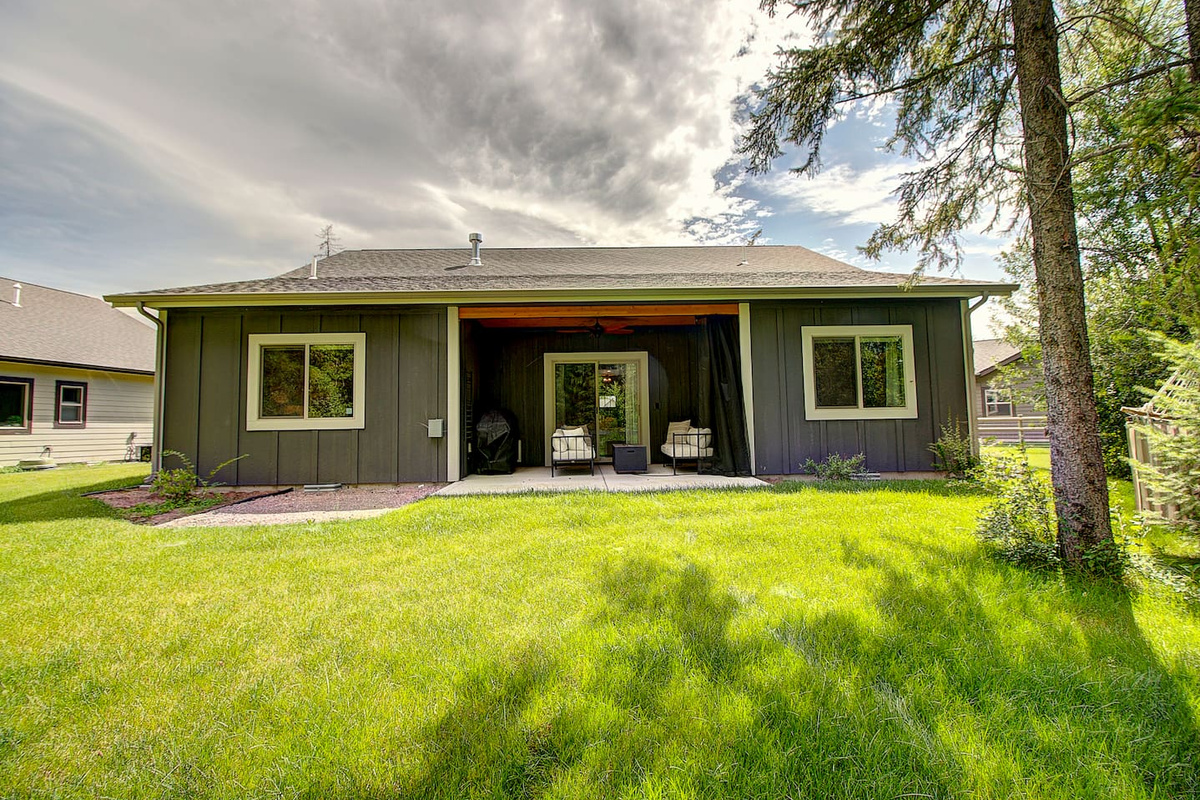 A covered patio with cozy seating opens up to a spacious green lawn, perfect for grilling out or just soaking up the Montana sunshine.