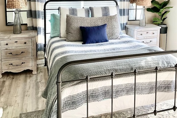 Rest easy in this coastal-inspired retreat. Featuring a classic wrought iron bed frame, plush nautical bedding, and rustic wood nightstands, this bright and airy room provides a peaceful sanctuary for a perfect night's sleep.