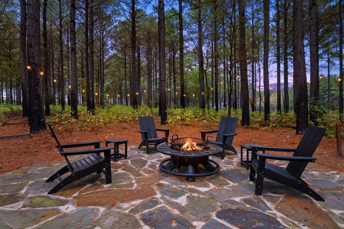 Stone firepit patio surrounded by tall pine trees.