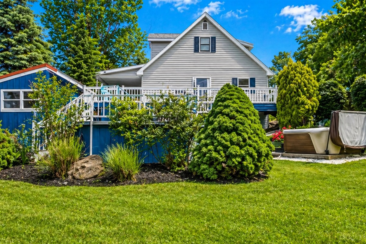This beautiful backyard features lush greenery, a relaxing hot tub, and a spacious deck, perfect for outdoor enjoyment.