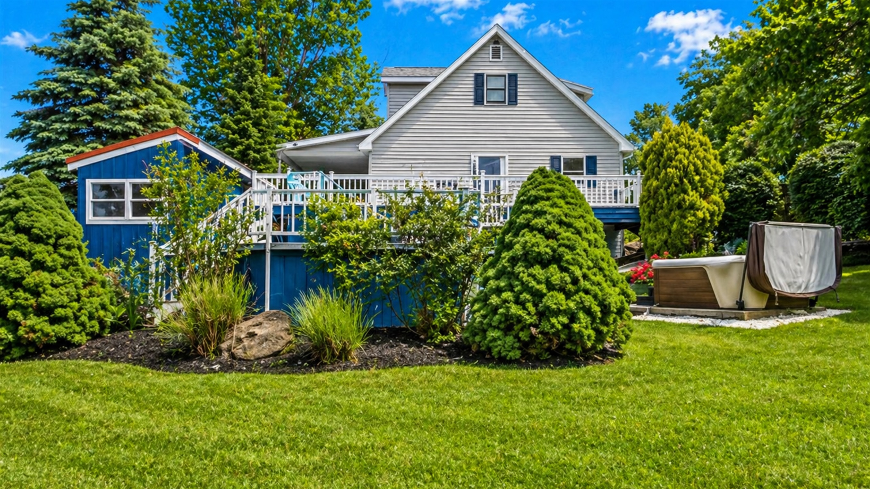 This beautiful backyard features lush greenery, a relaxing hot tub, and a spacious deck, perfect for outdoor enjoyment.