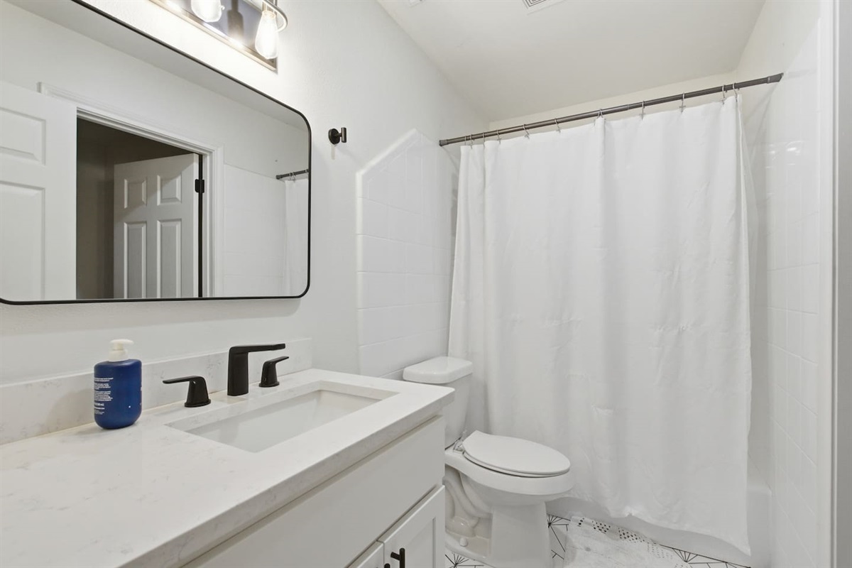 Bright full bathroom with bathtub and shower combo, modern vanity, fresh towels, and clean hotel-style finishes.