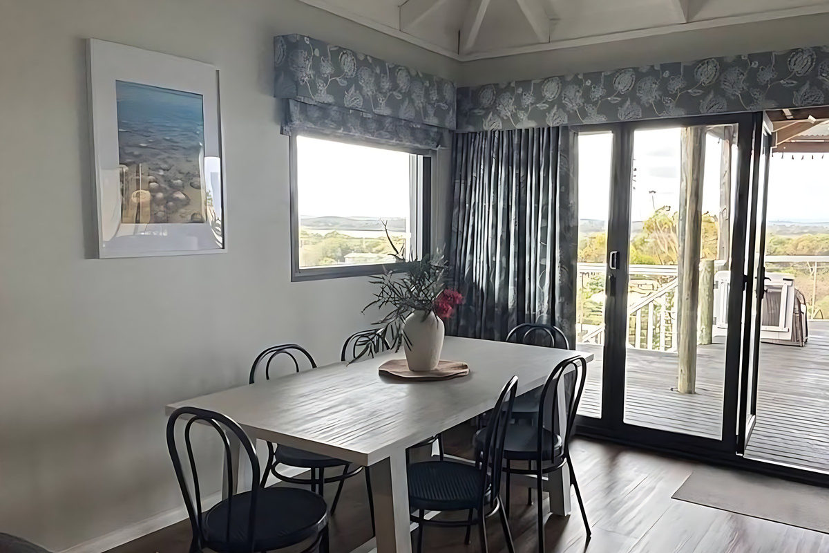 The dining table seats six beside sliding doors to the gazebo deck, with a window framing Lake Preston and Yalgorup National Park beyond the treetops of Preston Beach.