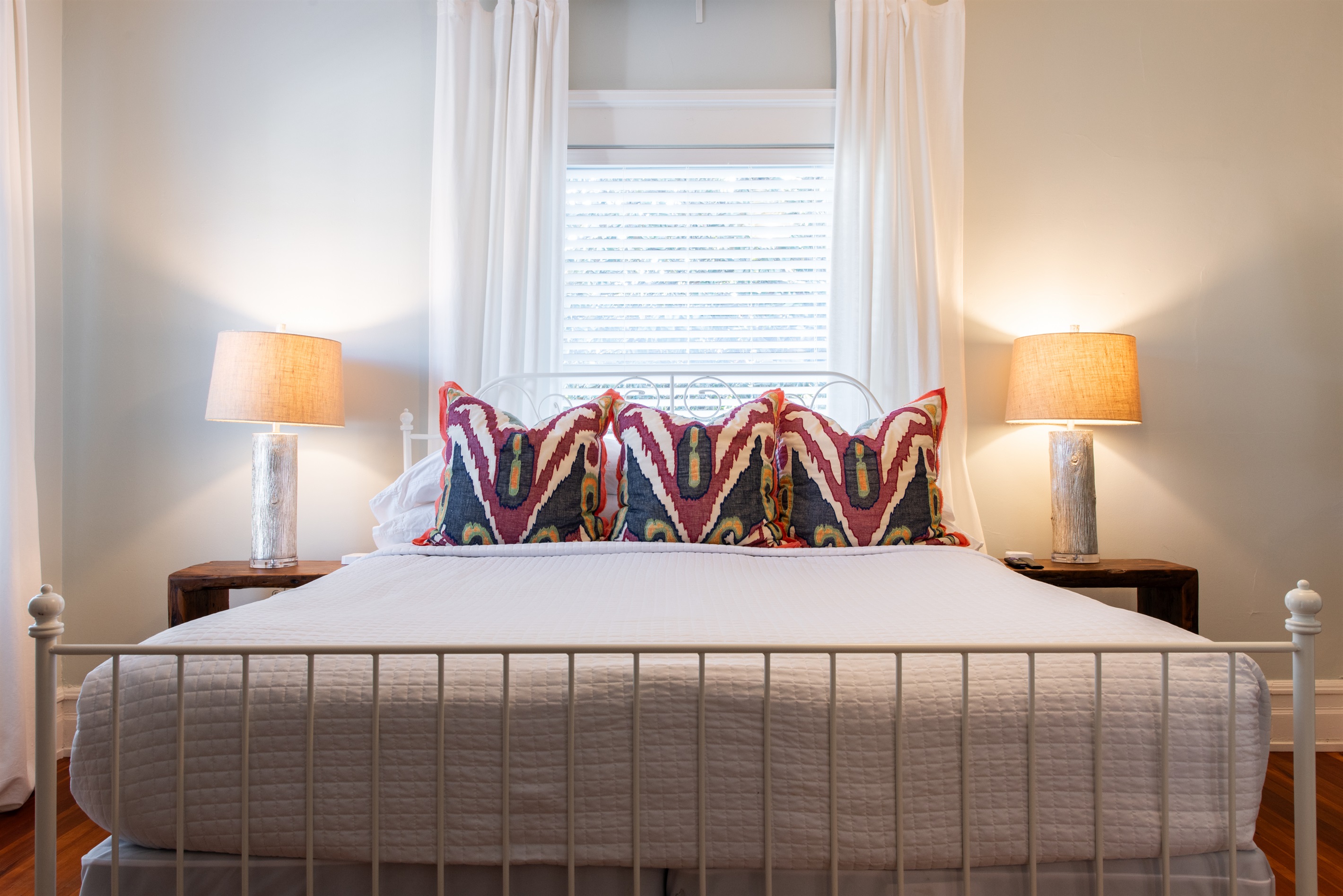 Rest in this bright bedroom on the Bourbon Trail in Louisville’s Highlands! Features a cozy bed with vibrant pillows, nightstands with lamps, and a window view—perfect for a relaxing stay.