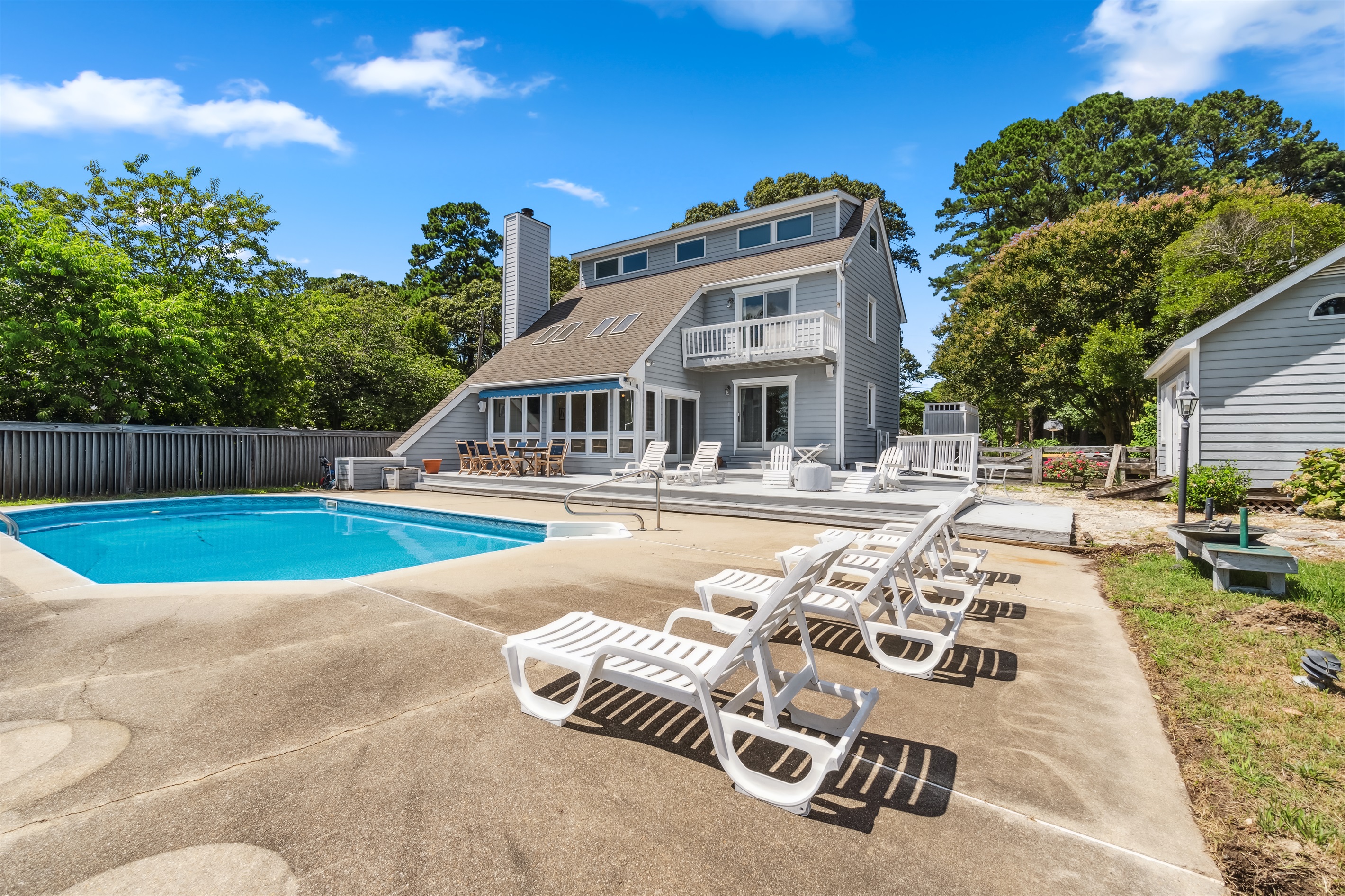 Sun soaked pool area with loungers, deck, and outdoor seating overlooking the home.