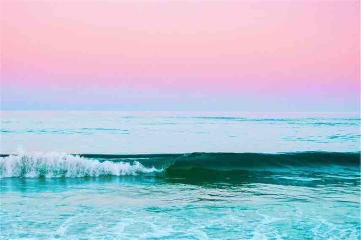 Tranquil ocean waves under soft pink and blue skies evoke calm and serene beach vibes.
