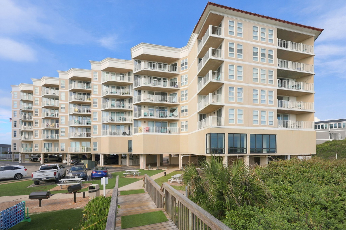 Exterior view of the resort building, featuring a wooden walkway and green lawn area.