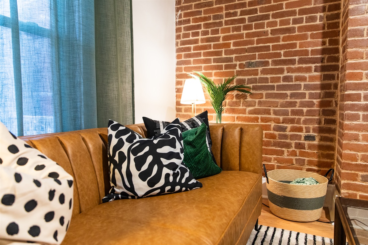 Cozy corner with leather sofa, bold pillows, and warm brick backdrop for a stylish retreat