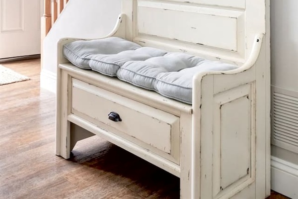 This charming, vintage-style hall tree bench provides a comfortable spot to sit and change shoes. Its distressed white finish and soft cushion add a touch of farmhouse style to the entryway.