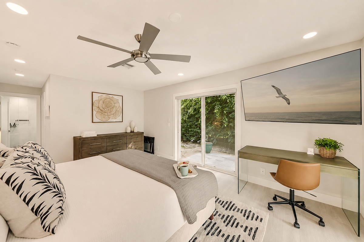 This bedroom adds extra comfort with a plush bed, TV, workspace, dresser, ceiling fan, and easy access to the patio.