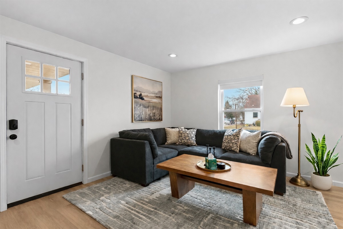 Unwind in this cozy living area featuring a plush sectional, warm wood accents, soft lighting, and natural light that creates a calm, inviting retreat.