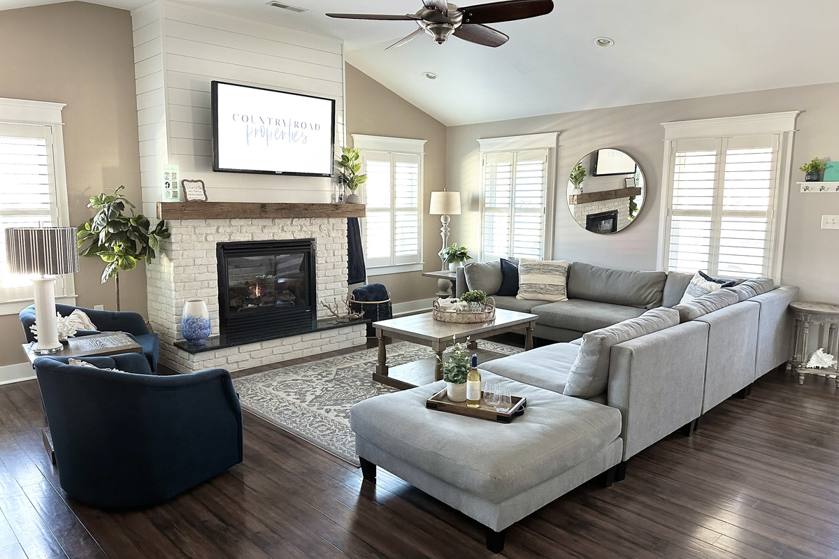 Relax in the bright, airy living room featuring a cozy white brick fireplace, a massive sectional, and stylish navy armchairs. It’s the ultimate space for family movie nights or wine by the fire during your dream getaway.