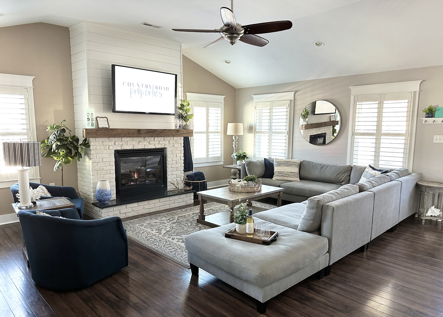 Relax in the bright, airy living room featuring a cozy white brick fireplace, a massive sectional, and stylish navy armchairs. It’s the ultimate space for family movie nights or wine by the fire during your dream getaway.