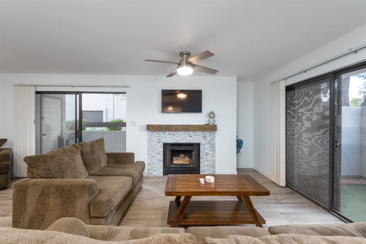 Living room with soft seating, a fireplace, wall-mounted TV, and patio doors on both sides.

