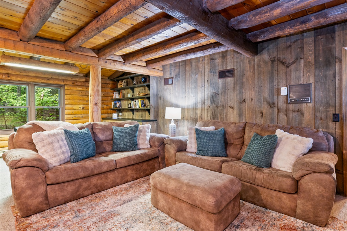 Charming log cabin living room featuring exposed beams, a grand stone fireplace, and plush seating for ultimate relaxation.